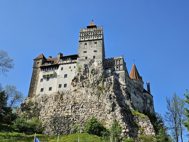 Bran Castle on a rocky cliff under a clear blue sky.