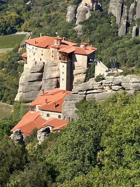 Monastery on a cliff amid lush green trees.