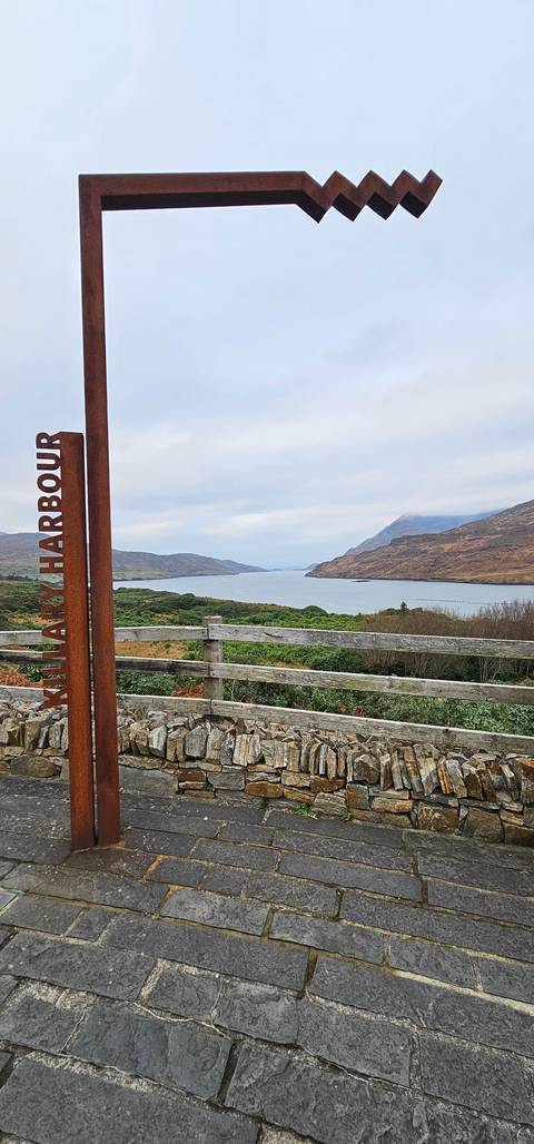 Vertical sign with waterfront view and mountainous backdrop.