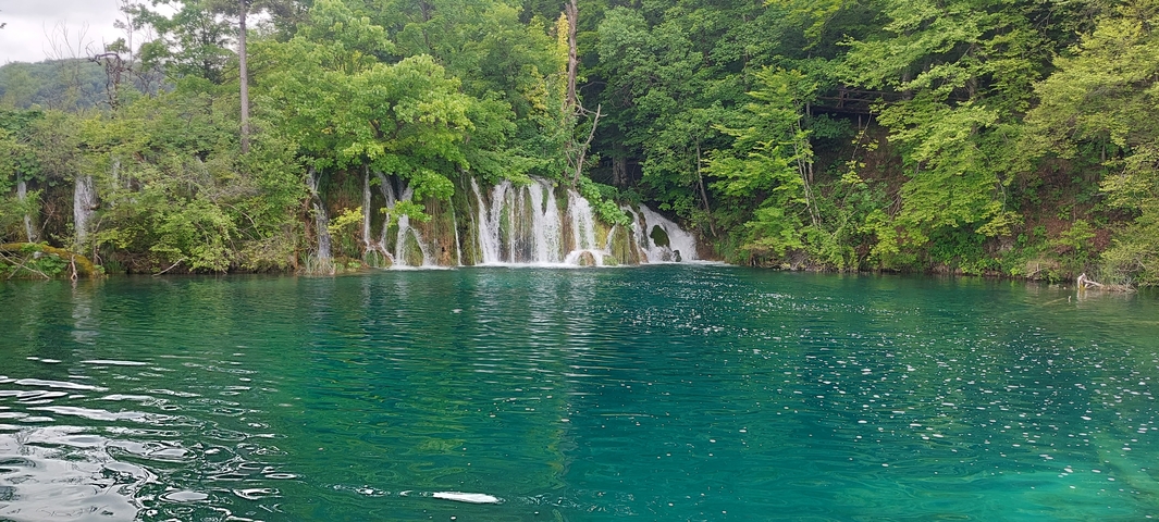 Serene waterfall flowing into a clear turquoise lake.