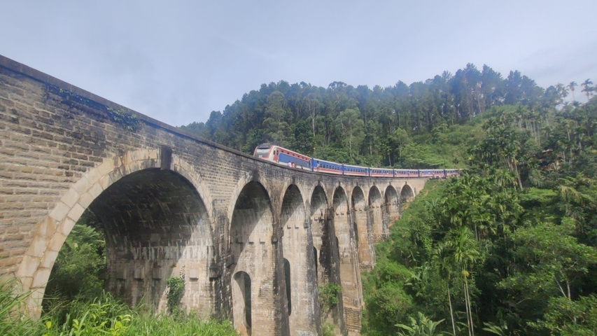 Train crossing a scenic stone bridge in a wooded area.