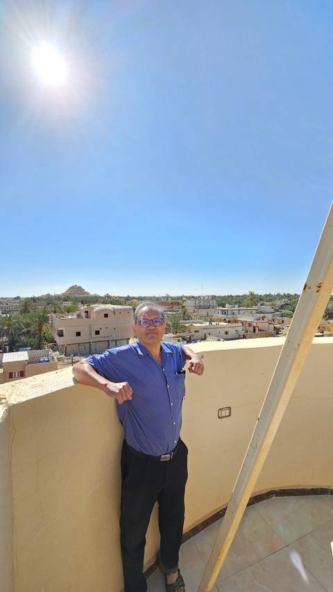 Person posing on a balcony with bright clear sky.