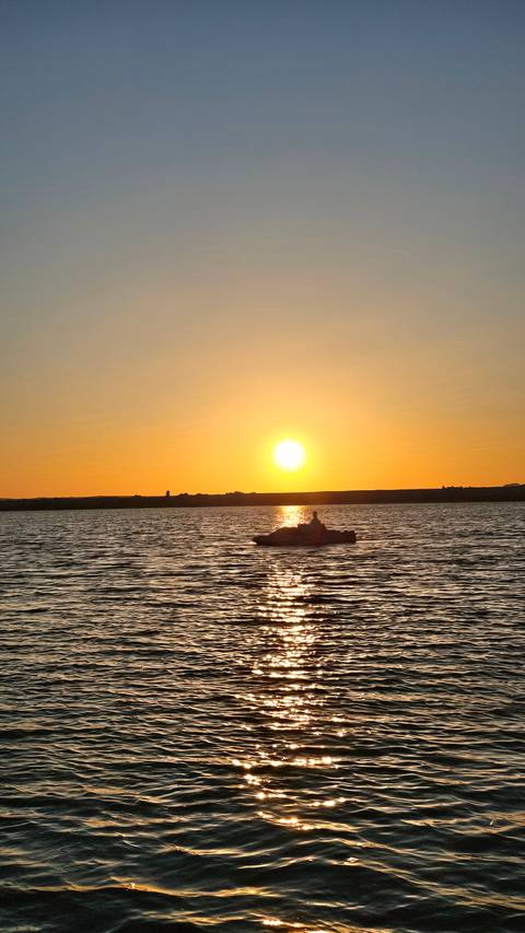 Silhouette of a boat against a sunset on the water.