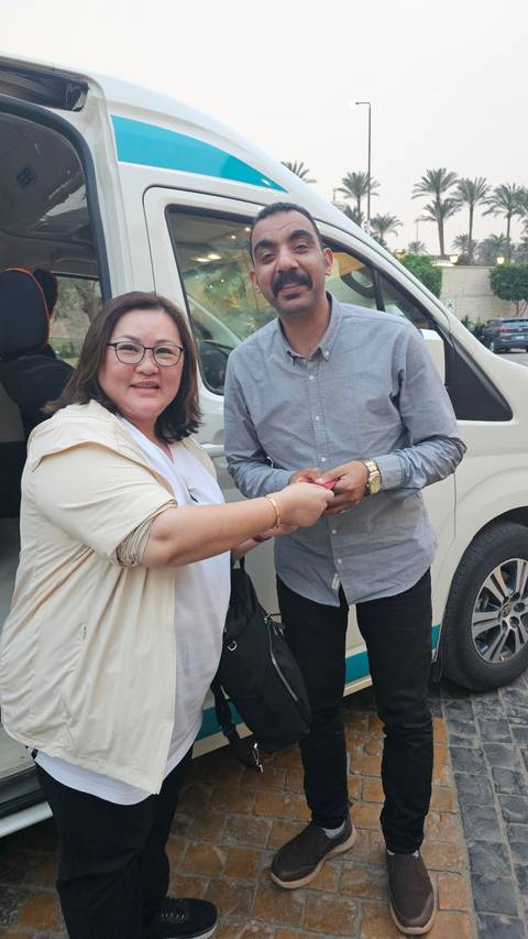 Two people shaking hands in front of a vehicle.