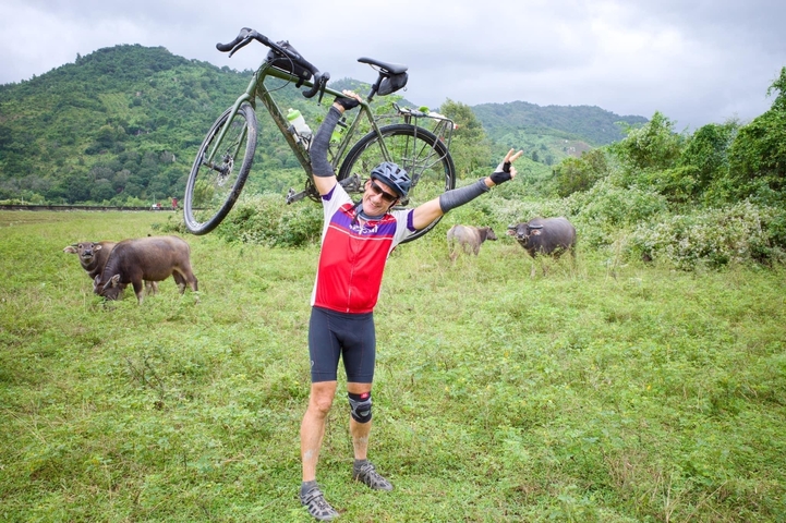 Cyclist posing with a bicycle in a field.