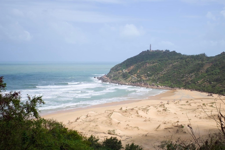 Sandy beach with waves and a distant lighthouse.