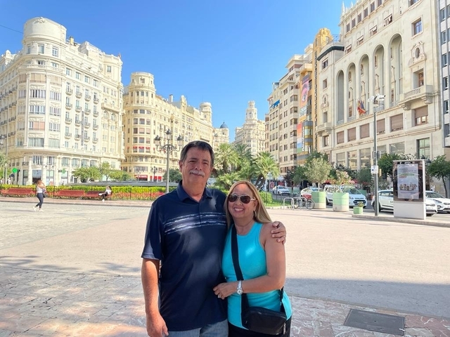 A couple smiling in front of elegant buildings in a city square.