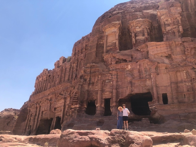 Ancient structure carved into red rock with two people posing.