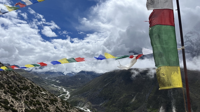 Mountainous landscape with colorful prayer flags against a cloudy sky.