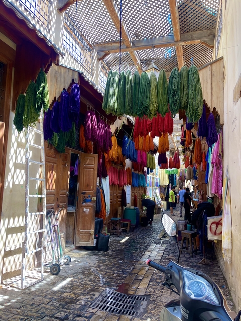 Market alley with hanging textiles and people walking.