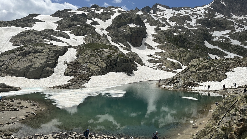 A lake surrounded by snowy mountains with some people around.