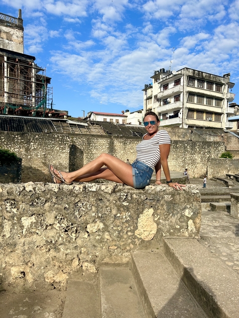 Person sitting on a stone wall, historic buildings in the background.