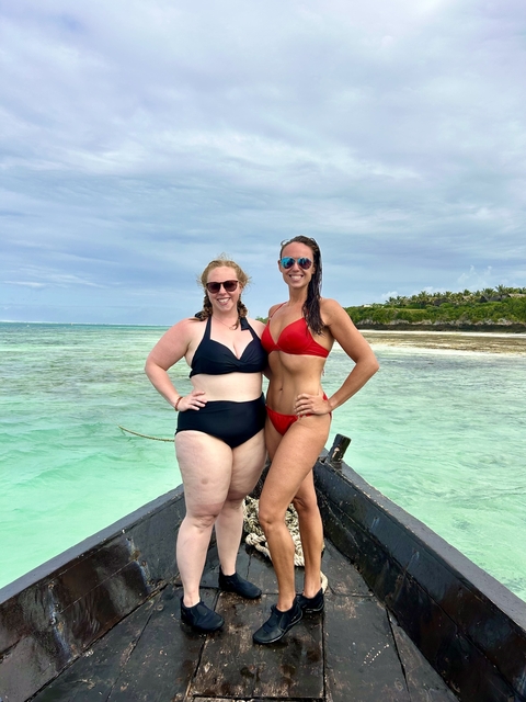 Two women in swimwear posing on a boat with clear ocean water.