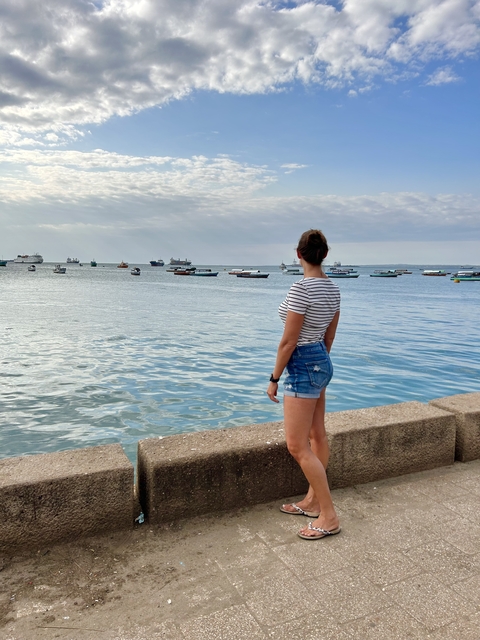 Woman looking out at boats in the ocean from a coastal promenade.