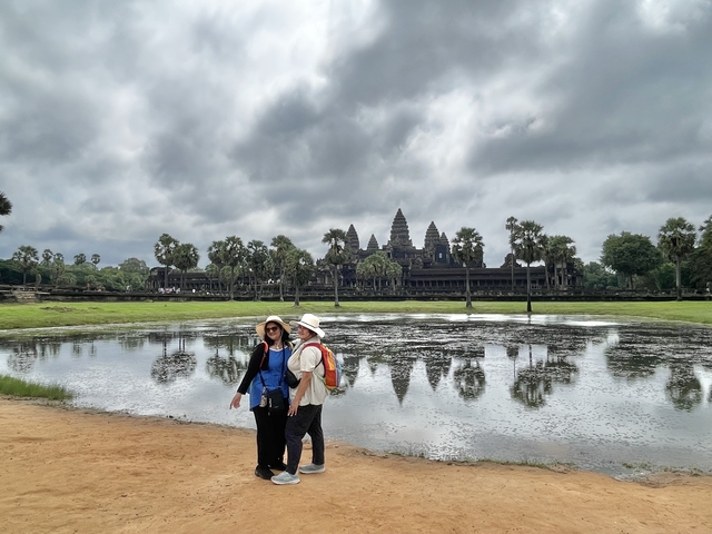People walking near a reflective pond with a temple in the background.
