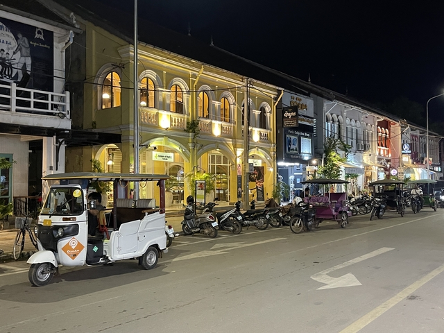 Tuktuks parked on a lit up street at night.