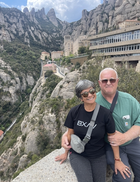 Two people smiling in front of a rocky mountain landscape.