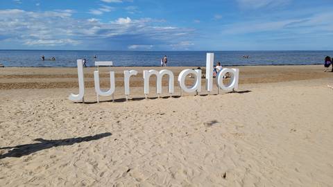 Beach with 'Jurmala' sign, people enjoying the sunny day.
