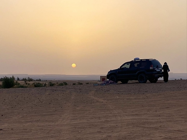 SUV parked in the desert with the sun near the horizon.