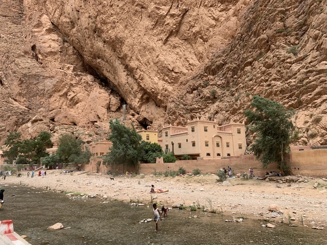 Buildings at the base of a rocky gorge with people and greenery.