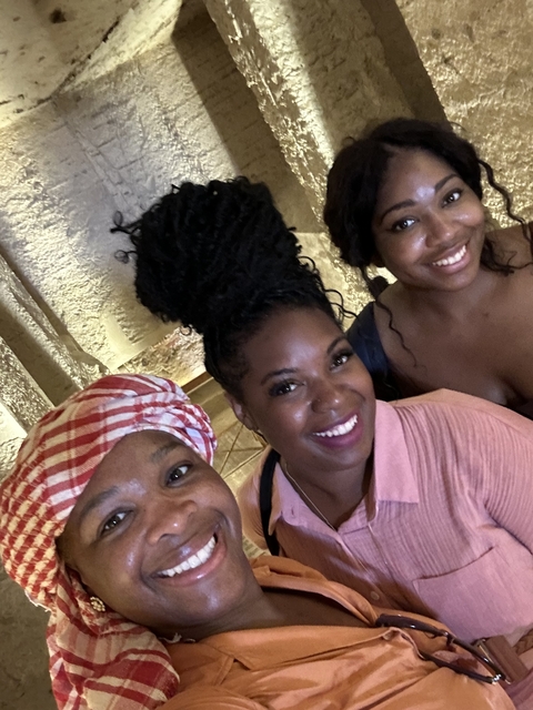 Three people smiling indoors in a historical site.