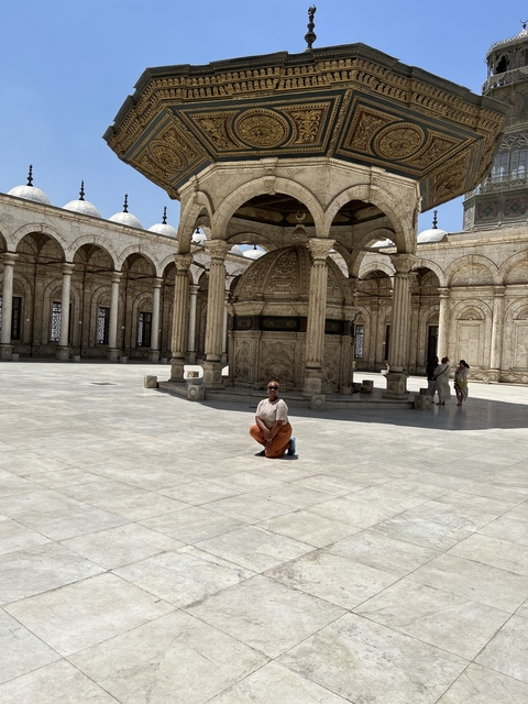 Person posing in a large courtyard with domed structure.