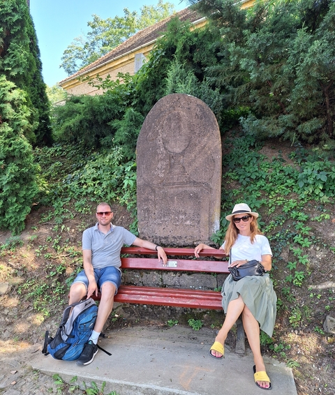 Two people seated on a bench next to an ancient stone monument.