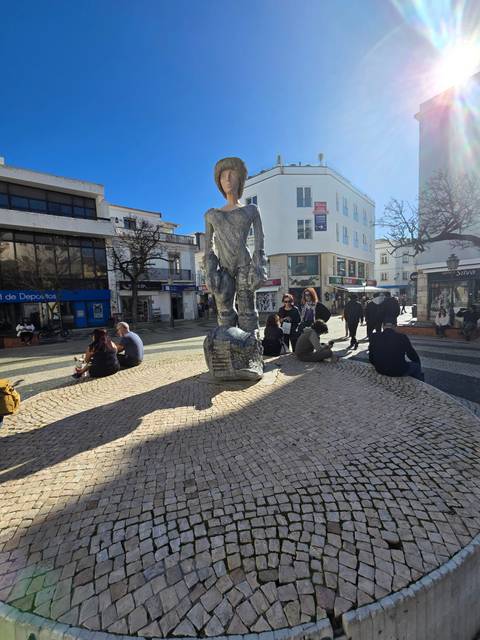 People sitting around a statue on a cobblestone square.