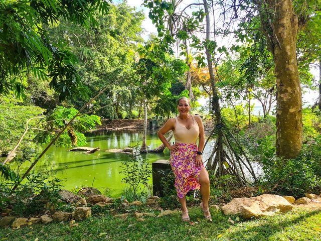 Woman posing by a lush green pond.