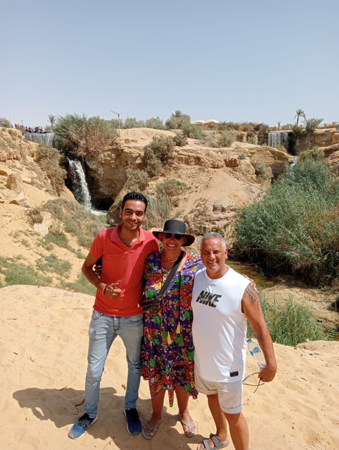 Three people posing with a waterfall and rocky landscape.