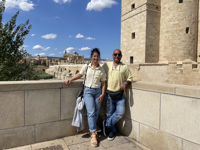 Two people standing on a bridge with historical buildings in the background.
