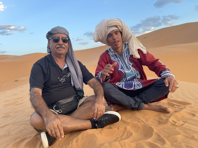Two people sitting on sand dunes with desert attire.