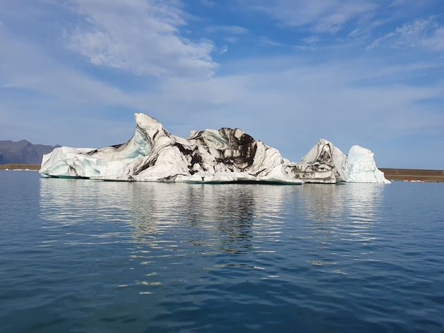 Iceberg with streaks of dark sediment reflected in calm waters.