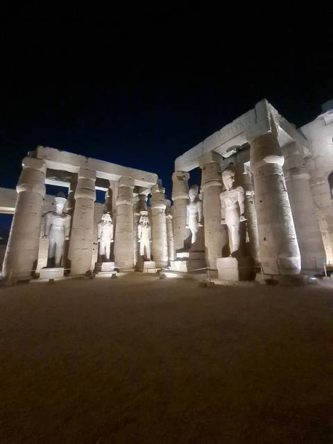 Statues on an illuminated ancient structure at night.