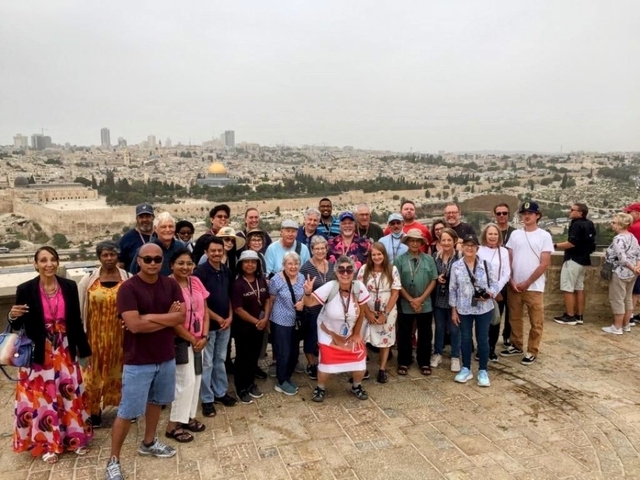 Group of tourists posing with a panoramic view of a cityscape.