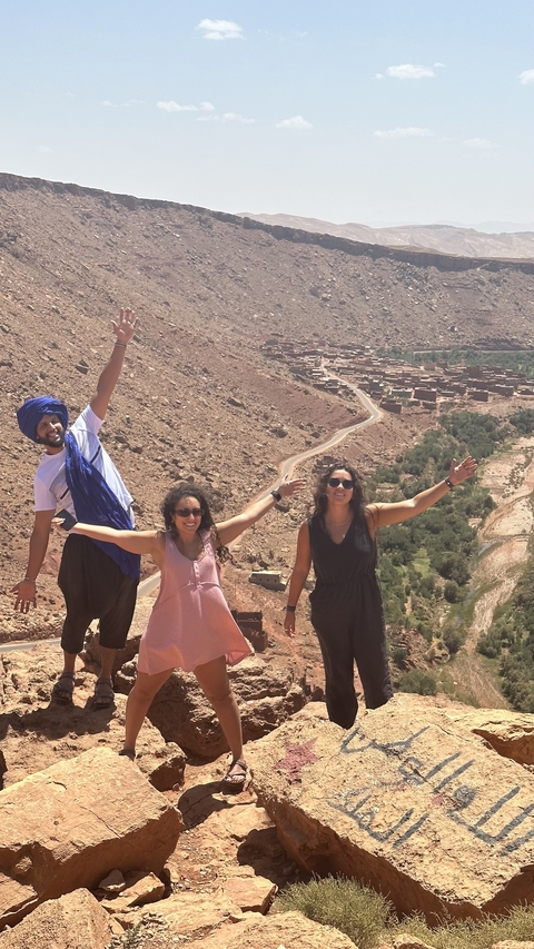 Three people posing on a rocky hill with a village below.