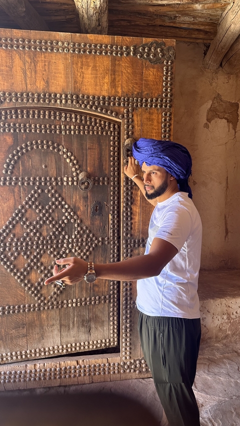 Man posing next to an ornate door wearing traditional attire.