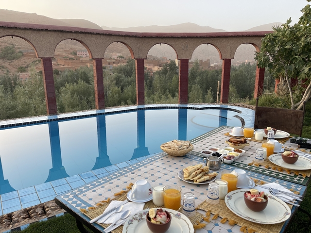 Breakfast table with food by a poolside with mountain views.