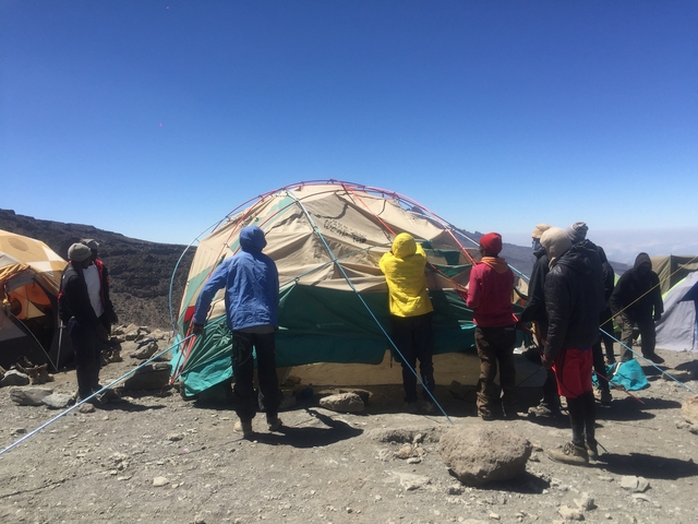 Group of people setting up a large tent at high altitude.