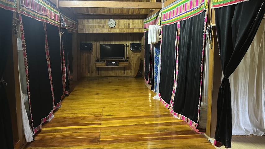 Interior view of a wooden room with black and colorful curtains and a television.