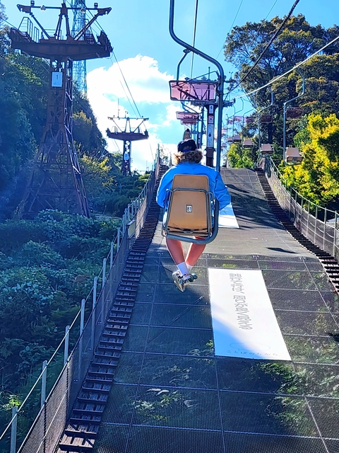 A person on a ski lift surrounded by lush trees.