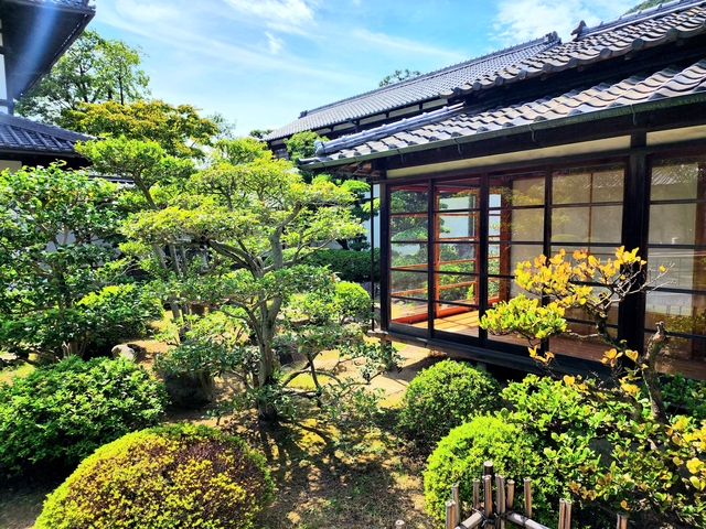 Japanese garden with lush bushes and a wooden structure.