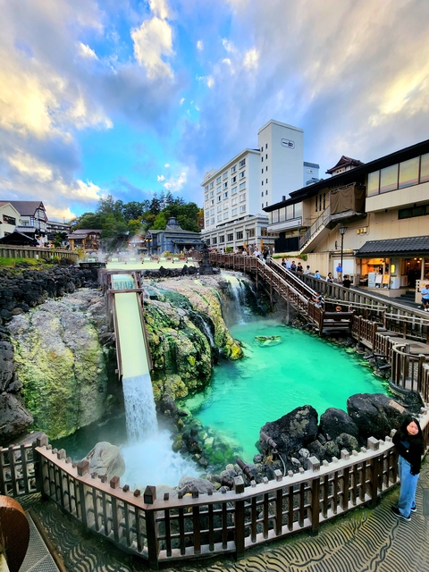 Hot spring with a waterfall and surrounding buildings.