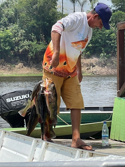Person holding multiple fishes near a river.