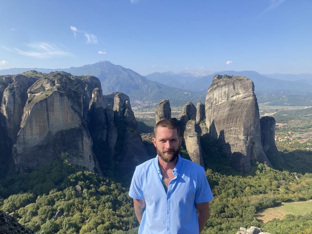 Man standing in front of towering rocky formations with scenic mountains.