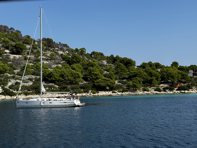 Sailboat on clear waters with lush green shoreline.