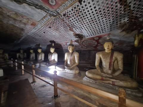 Buddha statues in a temple cave illuminated by lights.