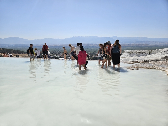 People wading in a travertine pool under a clear sky.