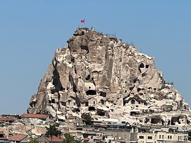 Rocky hill with ancient cave dwellings and a flag on top.