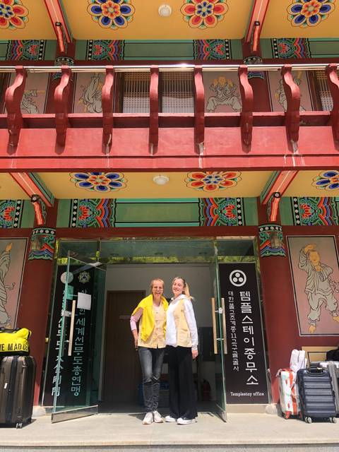 Two women standing in front of a colorful traditional building.